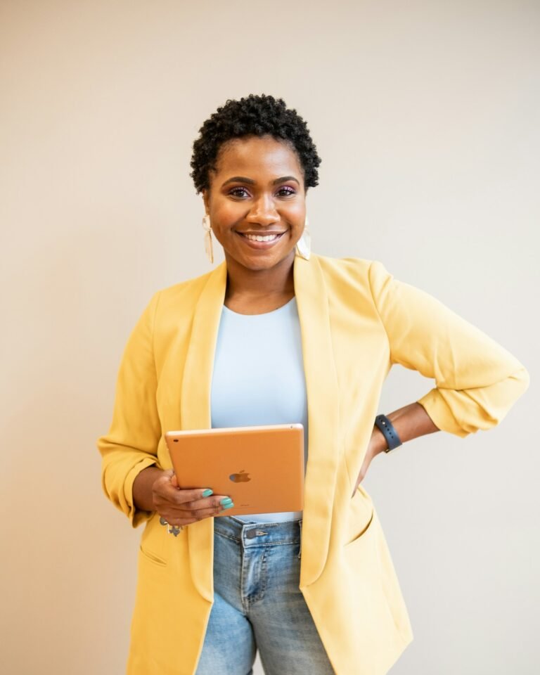 Femme souriante en blazer jaune tenant une tablette